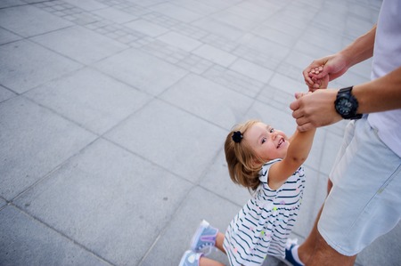 Young dad is playing with a charming little daughter. The man is holding the baby by the handles.の写真素材