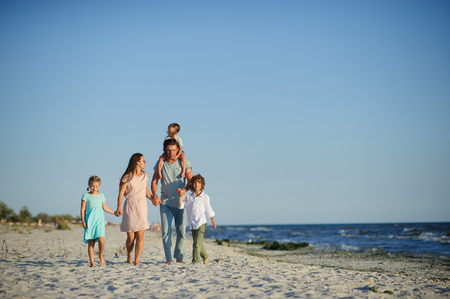 Big happy family walking at the beach. Mom, dad and three children. The blue sky, the sun, fresh sea wind. Pleasure from nature and communication.の写真素材