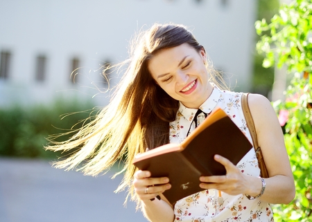 Cheerful young woman with long dark hair reads something. Summer sunny day, good weather. Woman has an excellent mood.の写真素材