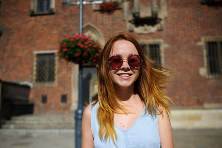 Charming girl in sunglasses against the backdrop of a beautiful old building. In her hand is a paper cup with coffee. The girl is smiling cheerfully.の写真素材