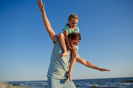 Young man gaily spends time with the little daughter by the sea.の写真素材