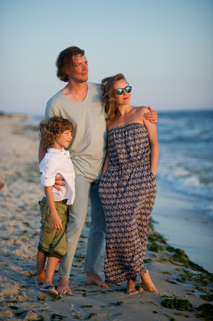 The young family admires a sunset on the sea coast. Light sea breeze. On faces pensive smiles.の写真素材