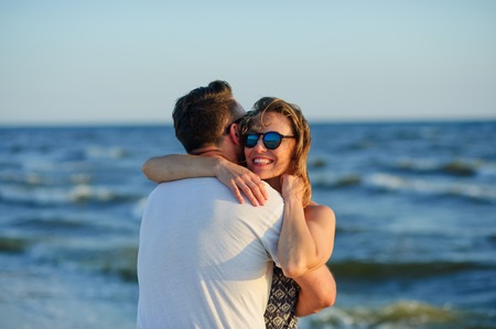 Man and woman hugging in the background of sea and sky. A man stands with his back to the camera, the woman's happy facial expression.の写真素材