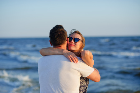 Man and woman hugging in the background of sea and sky. A man stands with his back to the camera, the woman's happy facial expression.の写真素材