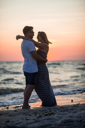 Couple of lovers stands having embraced on the seashore. Sunset, sea waves. Romantic appointment.の写真素材