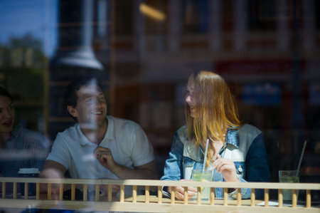 Three young friends behind glass of cafe. Two nice girls and guy. On a little table before them...