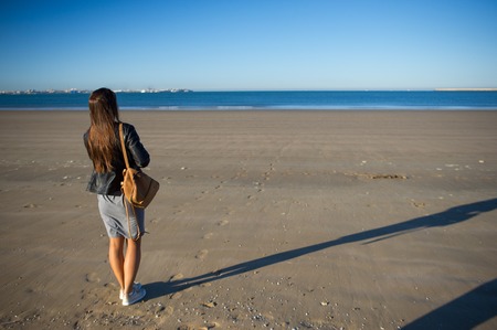 A woman admires the sea. She stands on the wet sand and stares into the distance. Blue sea, blue sky.の写真素材