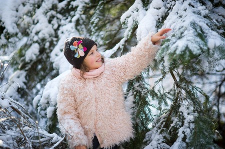 Portrait of the girl of 8-9 years in the winter park. The girl touches a snow-covered branch. From a frost of a cheek of the little belle became ruddy.の写真素材