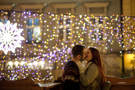 Lovers kiss on the background of shining festive garlands. Night. Romantic date.の写真素材