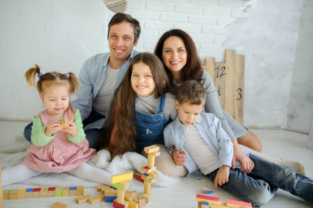 Day off in a big family. Dad, mom and three children are sitting on the floor. Younger children are built from tower cubes. Parents and the eldest daughter smile happily.の写真素材