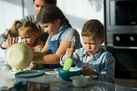 Mother and three children prepare something from the dough. Children like it very much. Their faces in flour, dough has stuck to hands.の写真素材
