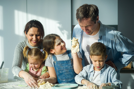 Large family prepares something of dough. Parents and three children at the kitchen table. Merry and useful pastime.の写真素材