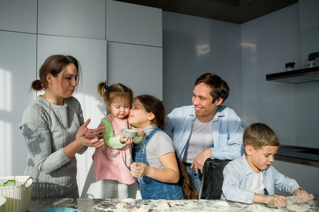 Large family prepares something of dough. Parents and three children at the kitchen table. Merry and useful pastime.の写真素材