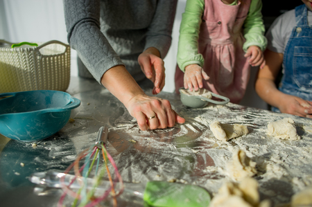 Mom teaches two little daughters to cook from dough. Children with pleasure are engaged in kitchen work.の写真素材