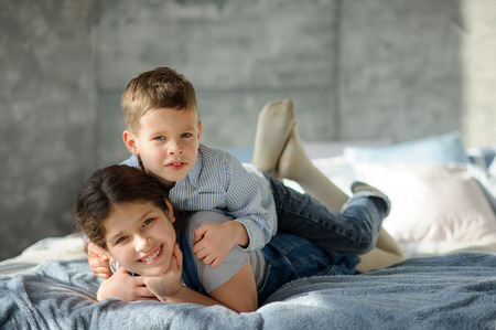 Two children, the boy and the girl, lie on a bed. The younger brother embraces elder sister for shoulders. Children have a good mood.の写真素材