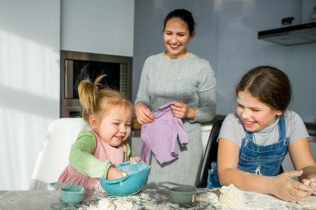 Mom teaches two little daughters to cook from dough. Children with pleasure are engaged in kitchen work.の写真素材