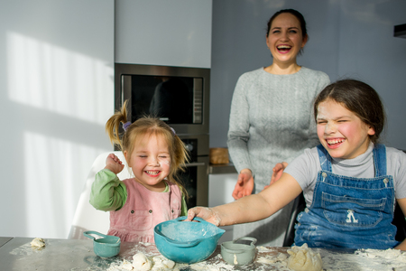 Mom teaches two little daughters to cook from dough. Children with pleasure are engaged in kitchen work.の写真素材