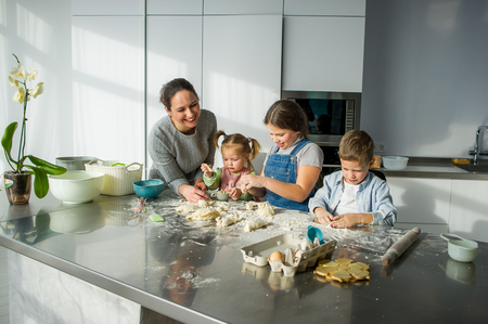 Mother teaches her three children to cook. Family is preparing something from the dough. There are necessary products on the kitchen table. Useful and fun pastime.の写真素材