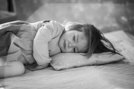 Little girl falls asleep on the bed. Baby is tired.の写真素材