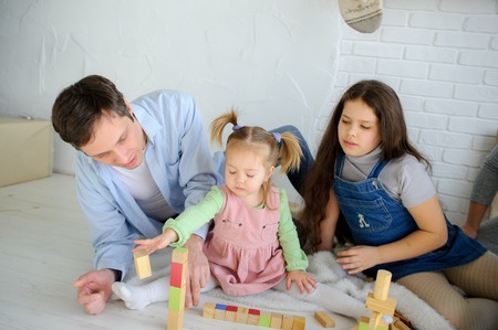 Father plays with two daughters. The man and the senior girl observe as the baby builds something of cubes.の写真素材