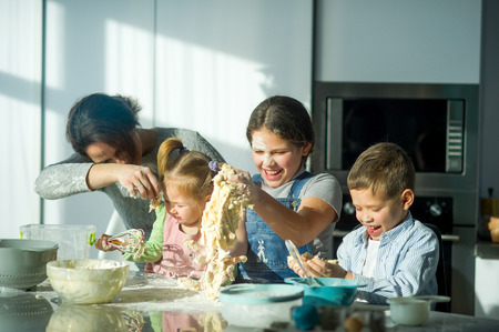 Mother teaches her three children to cook. Family is preparing something from the dough. There are necessary products on the kitchen table. Useful and fun pastime.の写真素材