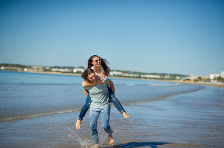 Young man holds on hands beautiful young woman. Couple spends time on the seashore. Summer, sea, good mood.の写真素材