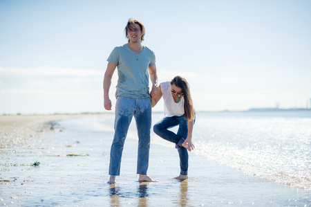 The young couple cheerfully spends time on the beach. The guy and the girl hold hands. Their clothes have got wet. The girl has pricked a leg.の写真素材