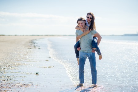 Young man holds on hands beautiful young woman. Couple spends time on the seashore. Summer, sea, good mood.の写真素材