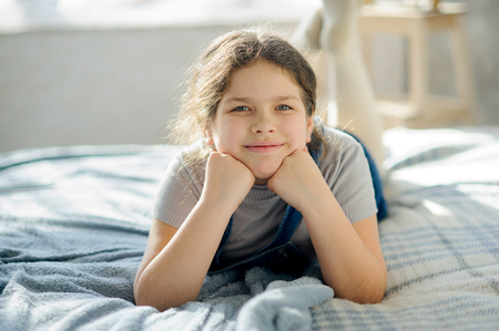 Portrait of a girl 10-11 years old. Child propped up hands head and looks at the camera with a dreamy smile.の写真素材