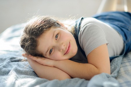 Portrait of a girl 10-11 years old. The child lies on the bed and looks at the camera with a dreamy smile.の写真素材