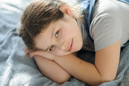 Portrait of a girl 10-11 years old. The child lies on the bed and looks at the camera with a dreamy smile.の写真素材