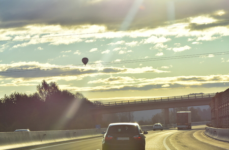 On the road. Vehicles on the highway in the morning sunlight with a balloon in the skyの写真素材