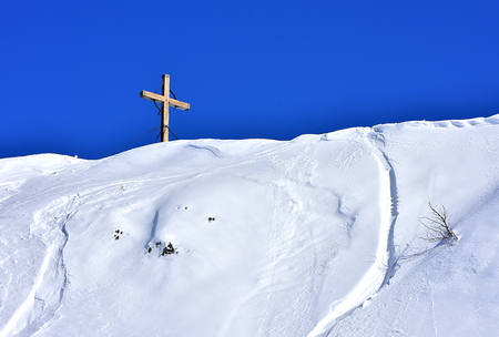 Beautiful view of the wooden cross that stands in the top of a snowy hill. With clear blue sky for the background. Vogel, Sloveniaの写真素材