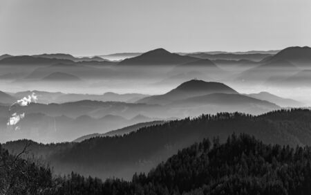 White and black photo. Horizontal landscape photo with hills and valleys.  Å aleÅ¡ka valley, Slovenia, winter afternoon. Represent pollution with smog.の写真素材