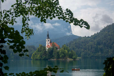Little Island with Catholic Church in Bled Lake, Slovenia at Sunrise with Castle and Mountains in Background.のeditorial素材