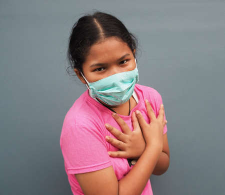 A girl wearing a protective mask While holding hands in the chest On a gray background.の写真素材