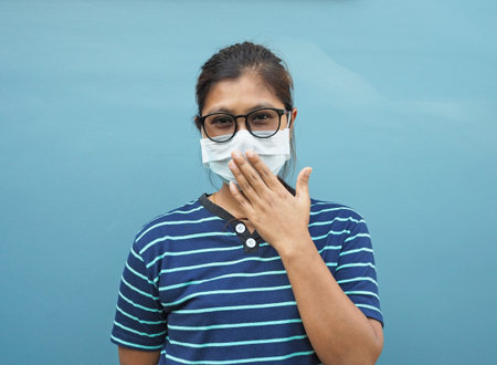 Portrait of Asian women wearing glasses and protective masks. While covering his mouth On a blue...
