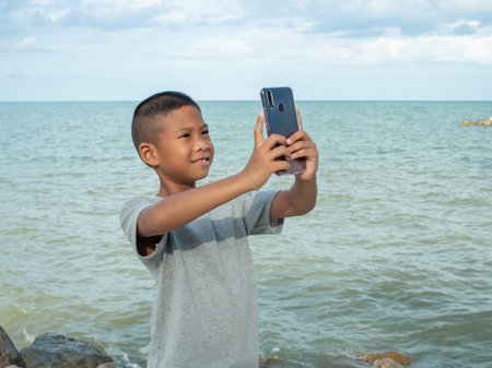 A boy using a phone to take a selfie on a sea background