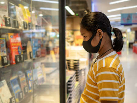 Long haired girl Wear a protective mask Looking at the showcase In a bookstore. Concept of life And protect yourself from the coronavirus outbreak.の写真素材