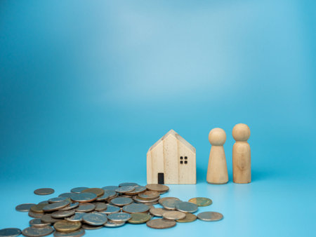 A wooden doll standing next to a replica wooden house and a pile of money has a blue background....