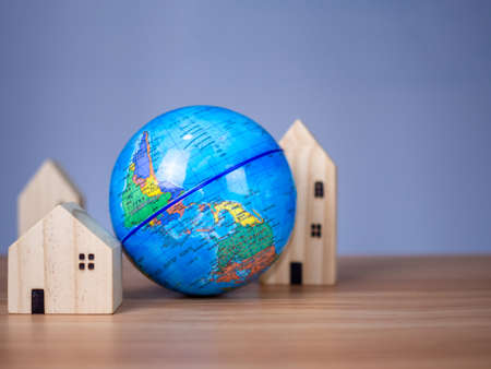 A wooden model house is placed beside a replica globe. placed on a wooden table with a light gray background. save world conceptの写真素材