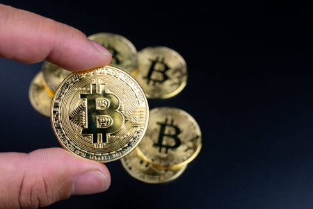 Human fingers holding bitcoins on a black background
