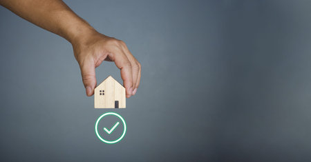 Concept of selling a house. A hand is holding a model house on a gray background. Real estate agent...
