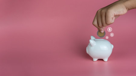 A human hand put a coin in a piggy bank on a pink background. Savings and investment concepts.の写真素材