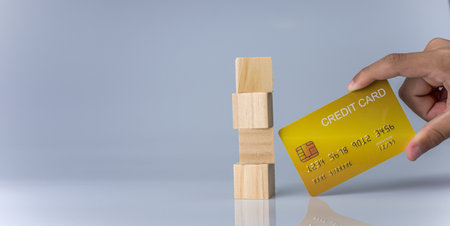 Hands holding credit cards and wooden cube blocks stacked on top of each other. Cashless spending concept.の写真素材