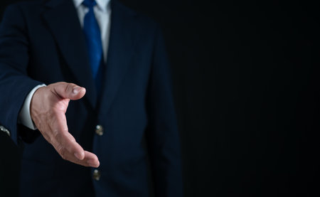 Businessman standing and doing handshake gesture on dark background. Business concept. Copy space.の写真素材