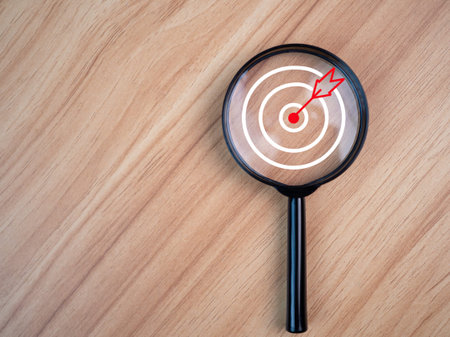 Magnifying glass with target icon placed on wooden table background. Business concept. Management...