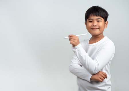 A boy in a white shirt is holding a white pen on a white background. Shows thinking, pondering, and considering options.の写真素材