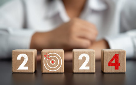 wooden blocks lined with year letters 2024 with a dart board and a businessman in the background It...