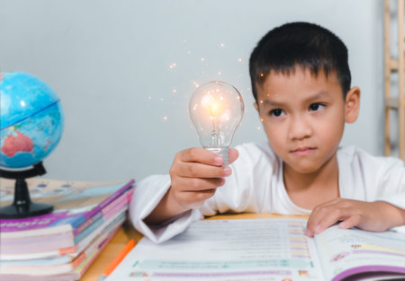 Education concept, Smart kid against green blackboard, Boy holding a bright light bulb to represent...